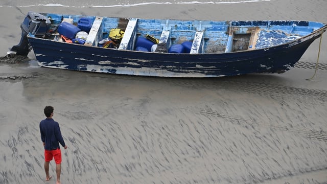 A Del Mar lifeguard looks over a capsized boat on the beach Monday at Torrey Pines State beach in San Diego, California.