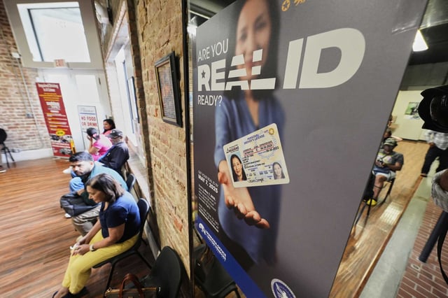 People wait inside a branch of the Louisiana Office of Motor Vehicles in Kenner, La., on Tuesday, next to signage about the Real ID card.