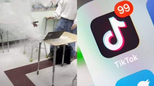 The image is a split-screen composite. On the left side, a school classroom scene shows a Chromebook placed on a desk emitting thick white smoke, with a student standing nearby—suggesting an ongoing battery fire. On the right side, a close-up of a smartphone screen displays the TikTok app with 99 notifications, referencing the viral nature of the trend behind the incident. Together, the image captures the real-world dangers of a destructive social media challenge spreading through TikTok.