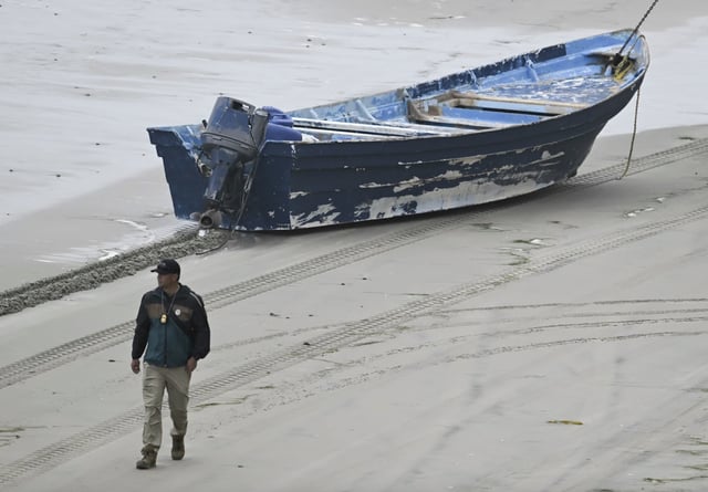 A law enforcement officer walks past the capsized boat at Torrey Pines State Beach in San Diego on May 5, 2025. 