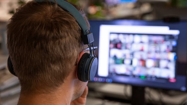Mann mit Kopfhörern vor Bildschirm mit virtuellem Meeting.
