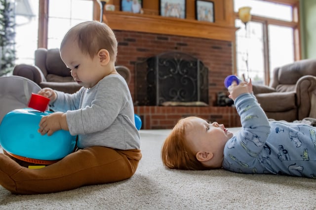 A 10 month old baby boy and a 9 month old baby girl sit on the floor close together and play with blocks