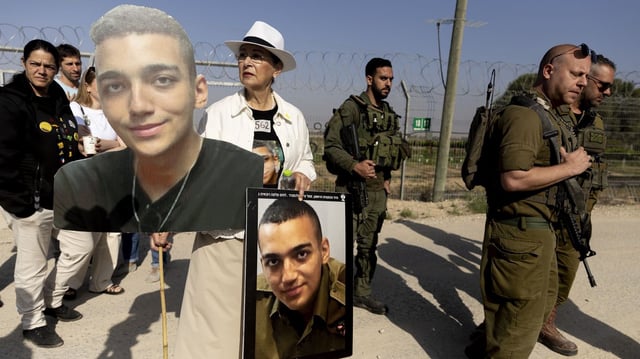 Varda Ben Baruch holds photos of her grandson Israeli- American hostage Edan Alexander as she walks near Israeli soldiers during a rally of families of hostages held in the Gaza Strip at Nir Oz near the border with the Gaza Strip. (Photo by Amir Levy/Getty Images)