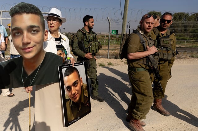 Varda Ben Baruch holds photos of her grandson Israeli- American hostage Edan Alexander as she walks near Israeli soldiers during a rally of families of hostages held in the Gaza Strip at Nir Oz near the border with the Gaza Strip on April 20, 2025 in Nir Oz, Israel.