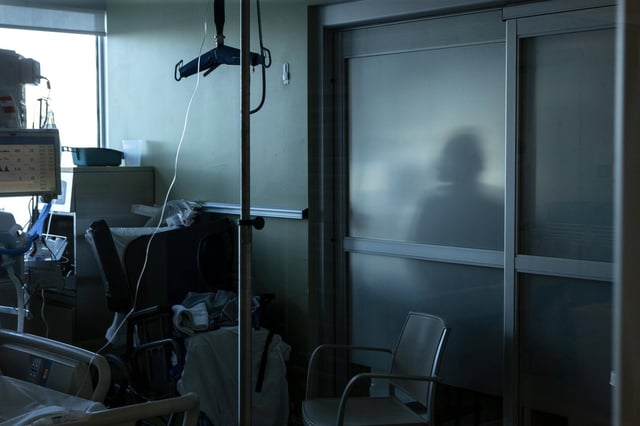 A nurse is silhouetted behind a glass panel as she tends to a patient in the Intensive Care Unit at an Ontario hospital on Tuesday, January 25, 2022. THE CANADIAN PRESS/Chris Young