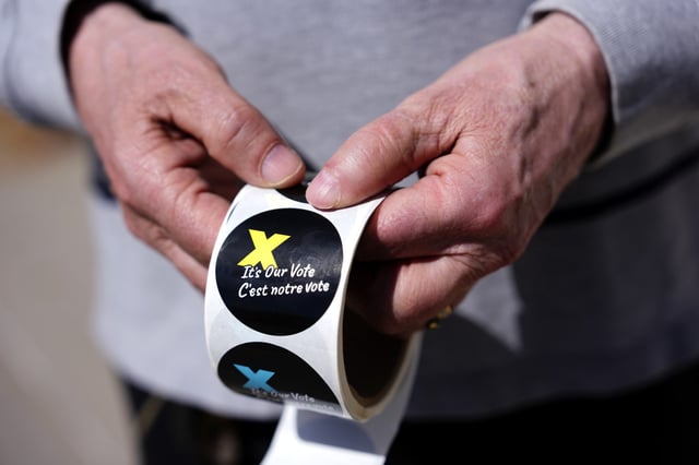 A voting information officer holds stickers to be given to voters after casting their ballots, outside a polling location in Ottawa on Monday, April 28, 2025. THE CANADIAN PRESS/Justin Tang