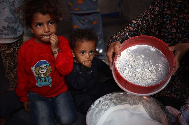 A displaced Palestinian woman sieves expired flour to remove mold and insects to make bread for her children in their displacement tent at the Yarmuk Sports Stadium, once a football arena, in Gaza City, on May 4, 2025.