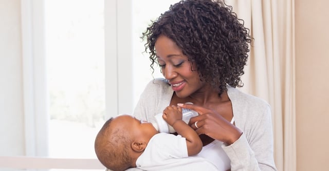 Happy mother feeding her baby boy his bottle at home in the bedroom
