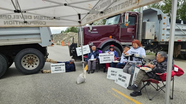 Splatsin members sit in front of dump trucks at the R.W. Bruhn Bridge site in Sicamous on May 12, 2025, calling for greater Indigenous participation in the construction project. 