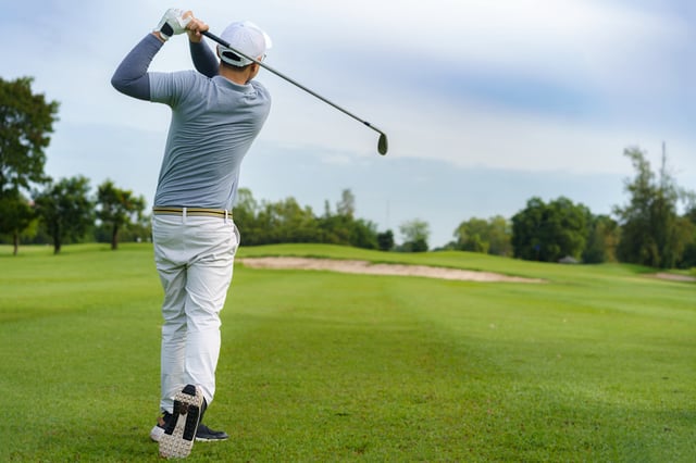 A golfer hitting golf ball along fairway with iron driver.