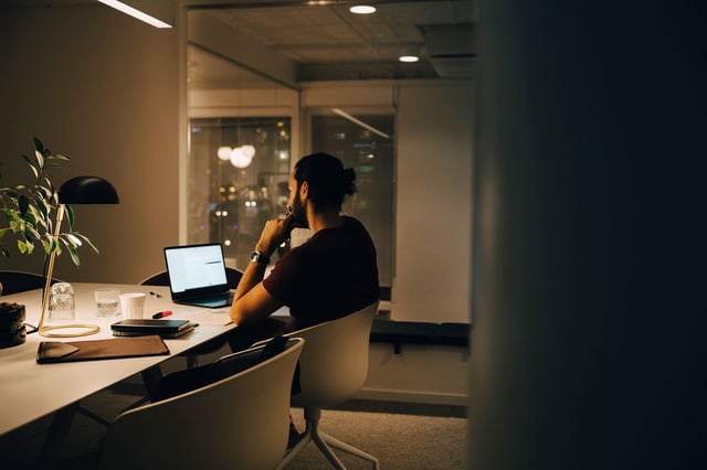 Side view of dedicated male professional working late at illuminated desk in coworking space