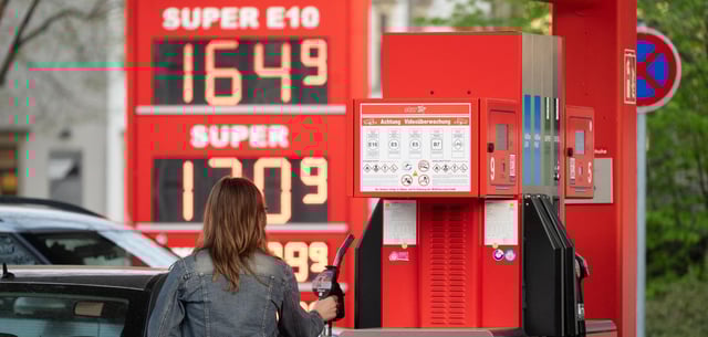 Eine Frau hält an einer Tankstelle vor einer Preistafel
