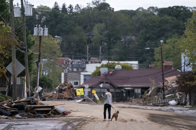 A woman walks her dog through Mary Grace and her dog among the wreckage and debris that Hurricane Helene left in Asheville, North Carolina.