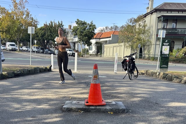 A person jogs near a traffic cone where a monument of British explorer Capt. James Cook once stood before it was removed following continued vandalism at a park Melbourne, Australia, Wednesday, May 14, 2025. (AP Photo/Rod McGuirk)