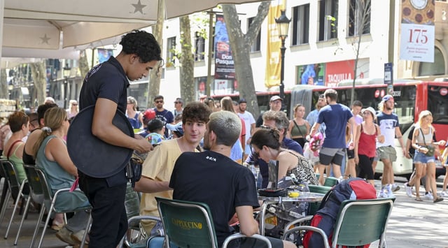 Un camarero cobra con tarjeta a unos clientes en una terraza frente al Liceu.