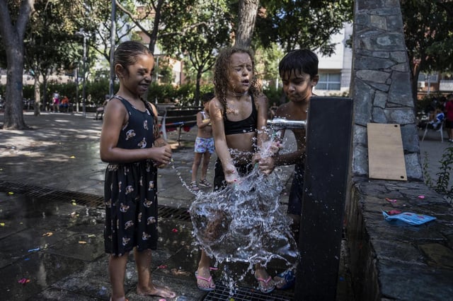 Tres niños juegan con el agua de una fuente del barrio de Santa Rosa, en Santa Coloma de Gramenet, una de las áreas vulnerables estudiadas.