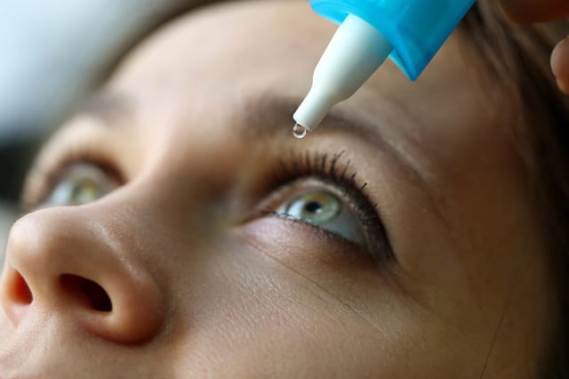 Female putting eye drops in her eye.