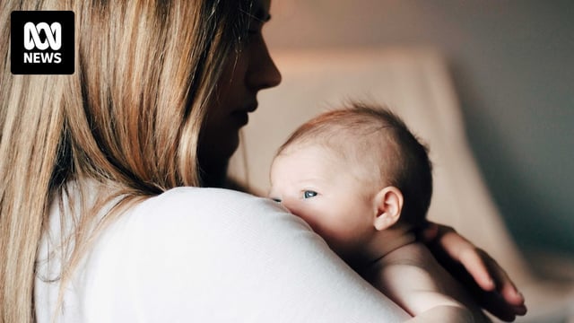 A newborn baby peeps over a woman's shoulder.