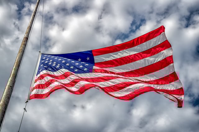 An American flag at half-staff blowing in wind with blue sky and clouds.