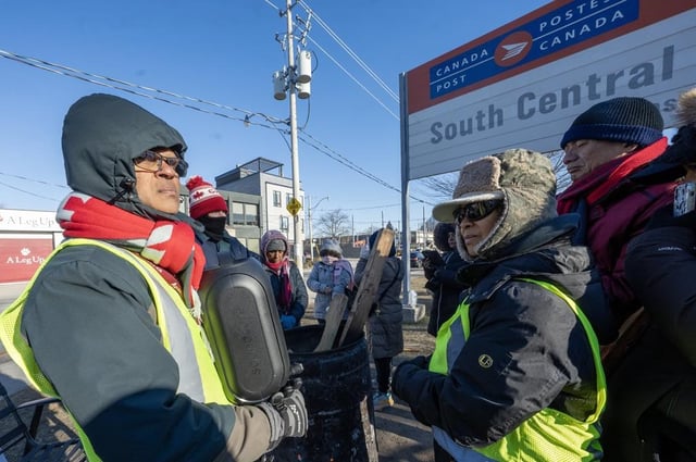 Striking Canada Post employees listen on a speaker to the news that Federal Labour Minister Steven MacKinnon is asking the Canada Industrial Relations Board to send the 50,000 employees back to work, in Toronto on Fri., Dec. 13, 2024. THE CANADIAN PRESS/Frank Gunn