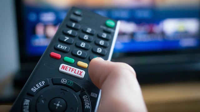 Using a television remote control with dedicated Netflix button, TV in the background.
