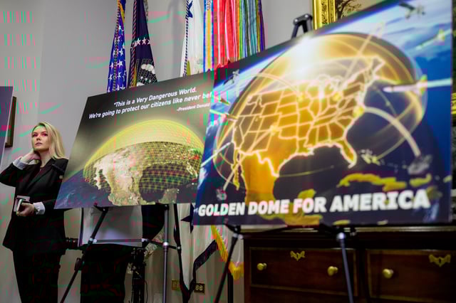 White House press secretary Karoline Leavitt looks on from behind a chart on prescription drug costs and posters depicting a &#34;Golden Dome for America&#34; as U.S. President Donald Trump speaks during a press conference in the Roosevelt Room of the White House on May 12, 2025, in Washington, DC.