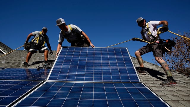 Three men install solar panels on the roof of a house in Camarillo, California.