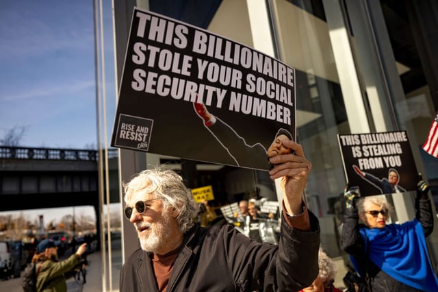 A protester holds signs that read 'This billionaire stole your social security number' during a protest at a Manhattan Tesla dealership to demonstrate against Tesla CEO Elon Musk, on March 13, 2025, in New York City.
