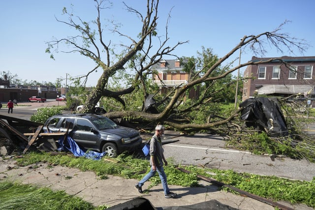 Eine Person geht an einem großen Baum vorbei, der eine Straße blockiert, nachdem ein heftiger Sturm in St. Louis durchgezogen ist.