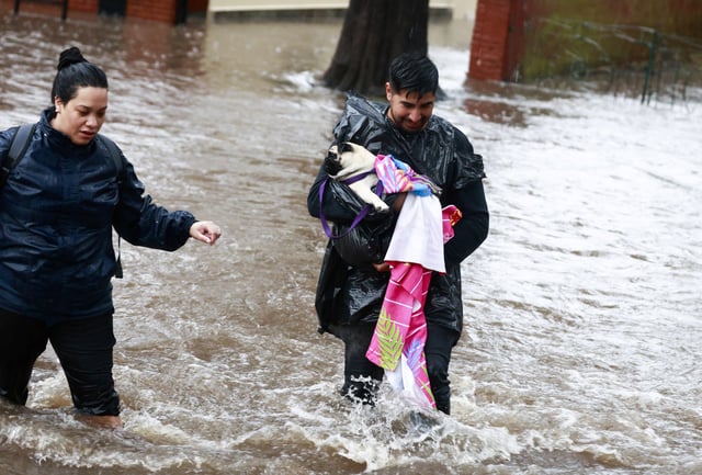 A man carries a dog as he walks amid flooding caused by heavy rains, in Capilla del Senor, in Buenos Aires, Argentina May 17, 2025. REUTERS/Matias Baglietto