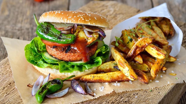 Veganer Burger mit Soja-Seitan-Patty und Grillgemüse mit Pimientos dazu  Pommes.