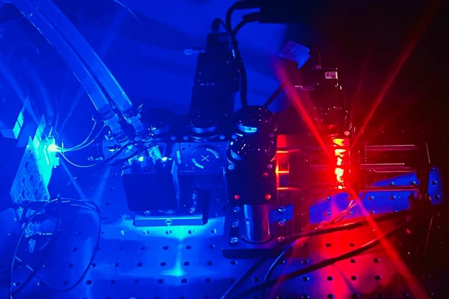 The researchers combined their suspended microchannel resonator (SMR) device with a fluorescent microscope (emitting blue light), which enables measurements of cell volume. The microscope is positioned at the entrance to the resonator, and cells flow through the device while floating in a fluorescent dye. This image shows a second-generation version of the device that can also measure cell shape.