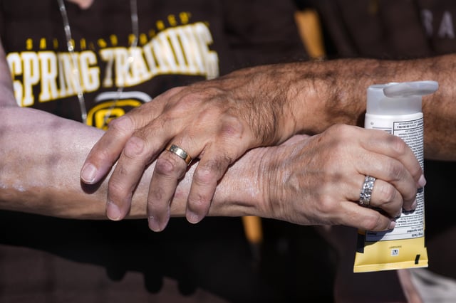 A man applies sunscreen to a woman's arm before a spring training baseball game between the San Diego Padres and the Chicago White Sox in Phoenix, Wednesday, Feb. 28, 2024. (AP Photo/Ashley Landis)