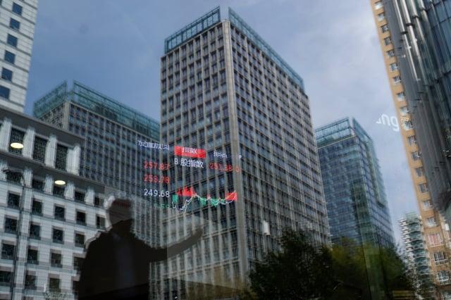 A person and buildings are reflected on the glass of a brokerage house where a display board is hung inside showing the stock index information, in Beijing, China April 9, 2025. REUTERS/Tingshu Wang/File Photo
