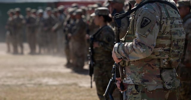 A member of the Texas National Guard looks down at his rifle ahead of the arrival of Gov. Greg Abbott and several other states leadership ahead of a press conference at Shelby Park in Eagle Pass on Feb. 04, 2024.
