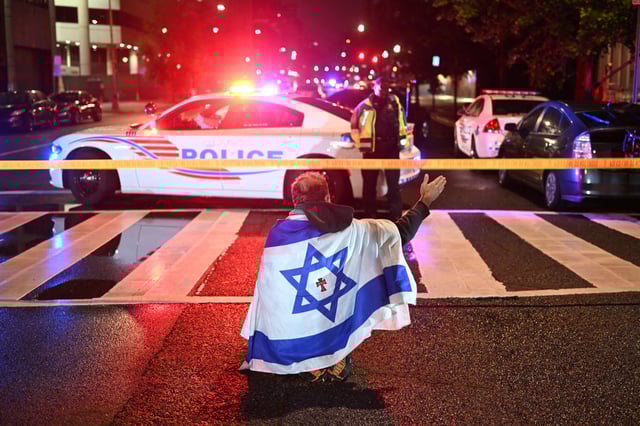 A man draped in the Israeli flag, bearing a cross and the name "Jesus" at its center, gestures as Metropolitan Police officers secure the area outside the Capital Jewish Museum following a shooting that left two people dead in Washington, D.C., in the early hours of May 22, 2025.