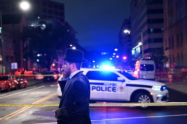 A man, standing behind police tape, talks on his cell phone outside the Capital Jewish Museum following a shooting that left two people dead, in Washington, DC, in the early hours of May 22, 2025.