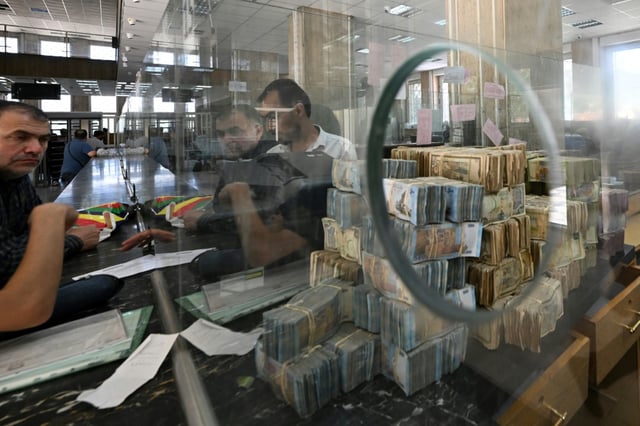 Bank notes of the local currency are piled up as people wait at the central bank in Damascus