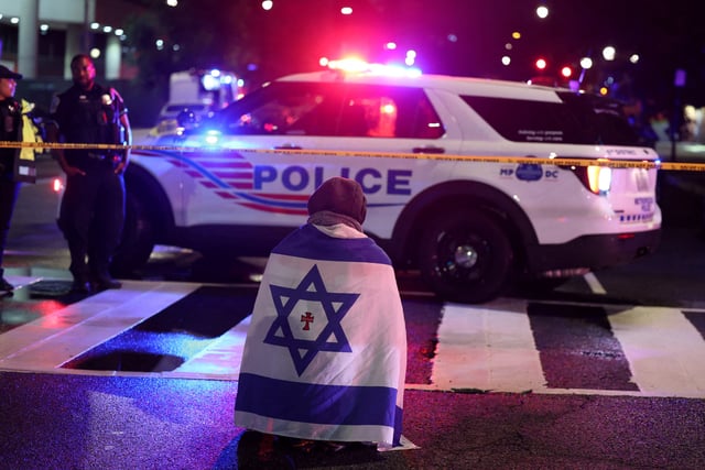 A man, with an Israeli flag with a cross in the center, kneels next to emergency personnel working at the site where, according to the U.S. Homeland Security Secretary, two Israeli embassy staff were shot dead near the Capital Jewish Museum in Washington, D.C., U.S. May 21, 2025.  REUTERS/Jonathan Ernst