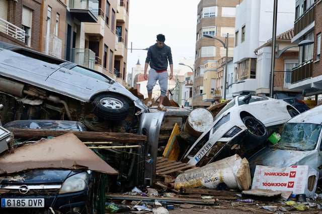 Un joven subido sobre una pila de coches arrastrados por la riada en una calle de Sedaví, el día después de la dana.