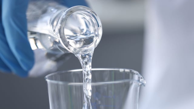 Scientist chemist in gloves pouring water from flask into glass closeup.