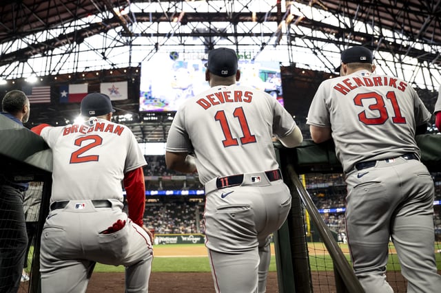 Alex Bregman #2 of the Boston Red Sox, Rafael Devers #11 of the Boston Red Sox, and Liam Hendriks #31 of the Boston Red Sox look on from the dugout before the Opening Day game against the Texas Rangers on March 27, 2025 at Globe Life Field in Arlington, Texas.