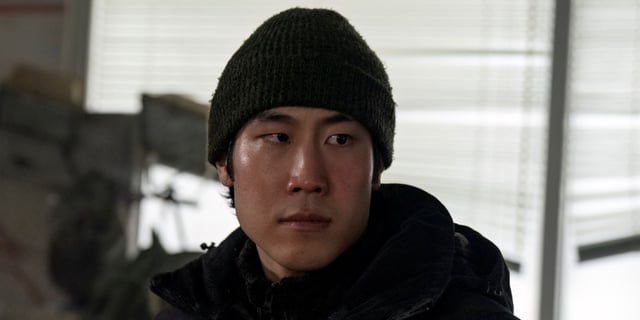 Young Mazino as Jesse looking off to the left in a black coat and a serious expression in The Last of Us Season 2