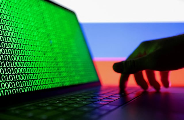 A hand is seen on a laptop with binary code displayed on the screen in front of a Russian flag in this picture illustration created on August 19, 2022. REUTERS/Dado Ruvic/Illustration/File Photo