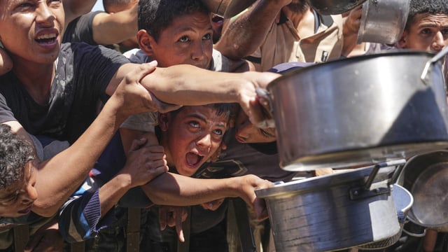 Palestinians struggle to receive cooked food distributed at a community kitchen in the Muwasi area of Khan Younis, in the Gaza Strip, Friday, May 23, 2025. 