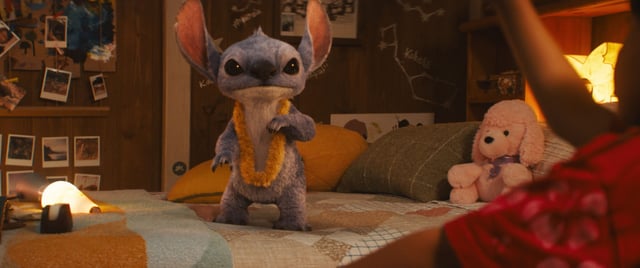 Stitch standing on a bed wearing a lei in the live-action &#39;Lilo &amp; Stitch&#39;.