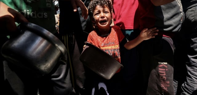 Un enfant pleure au milieu de Palestiniens qui attendent de recevoir un repas chaud distribué par une association caritative locale à Nousseirat, dans le centre de la bande de Gaza, le 24 mai 2025