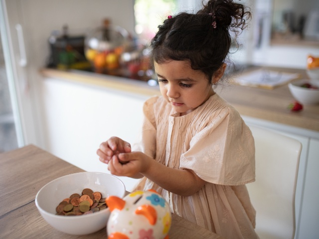 Little multiracial girl saving her money in to porcelain pig.