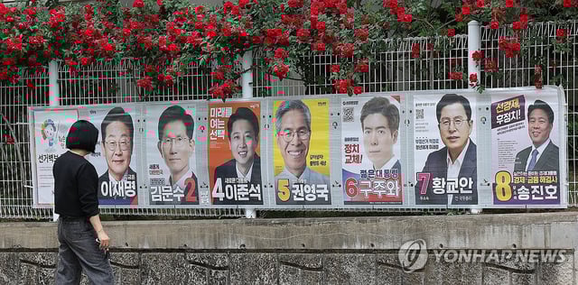 A pedestrian looks at the posters of presidential candidates on a wall in the southeastern city of Daegu on May 15, 2025. (Yonhap) 