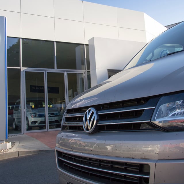 Car with Volkswagen logo in front of dealership building.